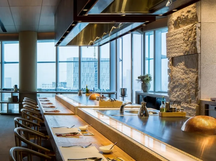 Modern industrial-style restaurant interior with wooden seating and glass walls showing a cityscape.