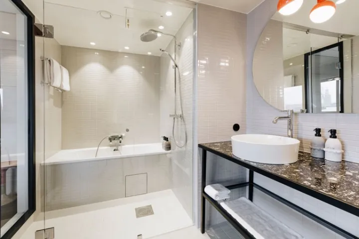 Modern minimalist bathroom with white tiles, a glass shower enclosure, a white countertop with a sink, and a large oval mirro
