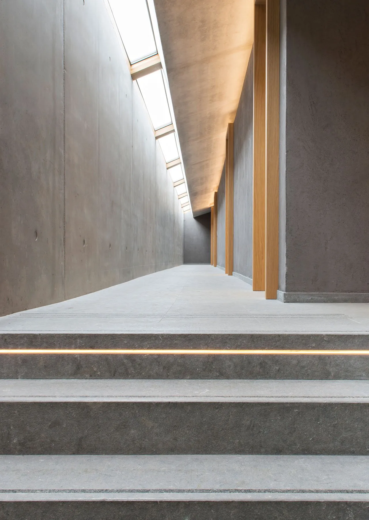 Modern, minimalist corridor with concrete walls and lit ceiling beams.