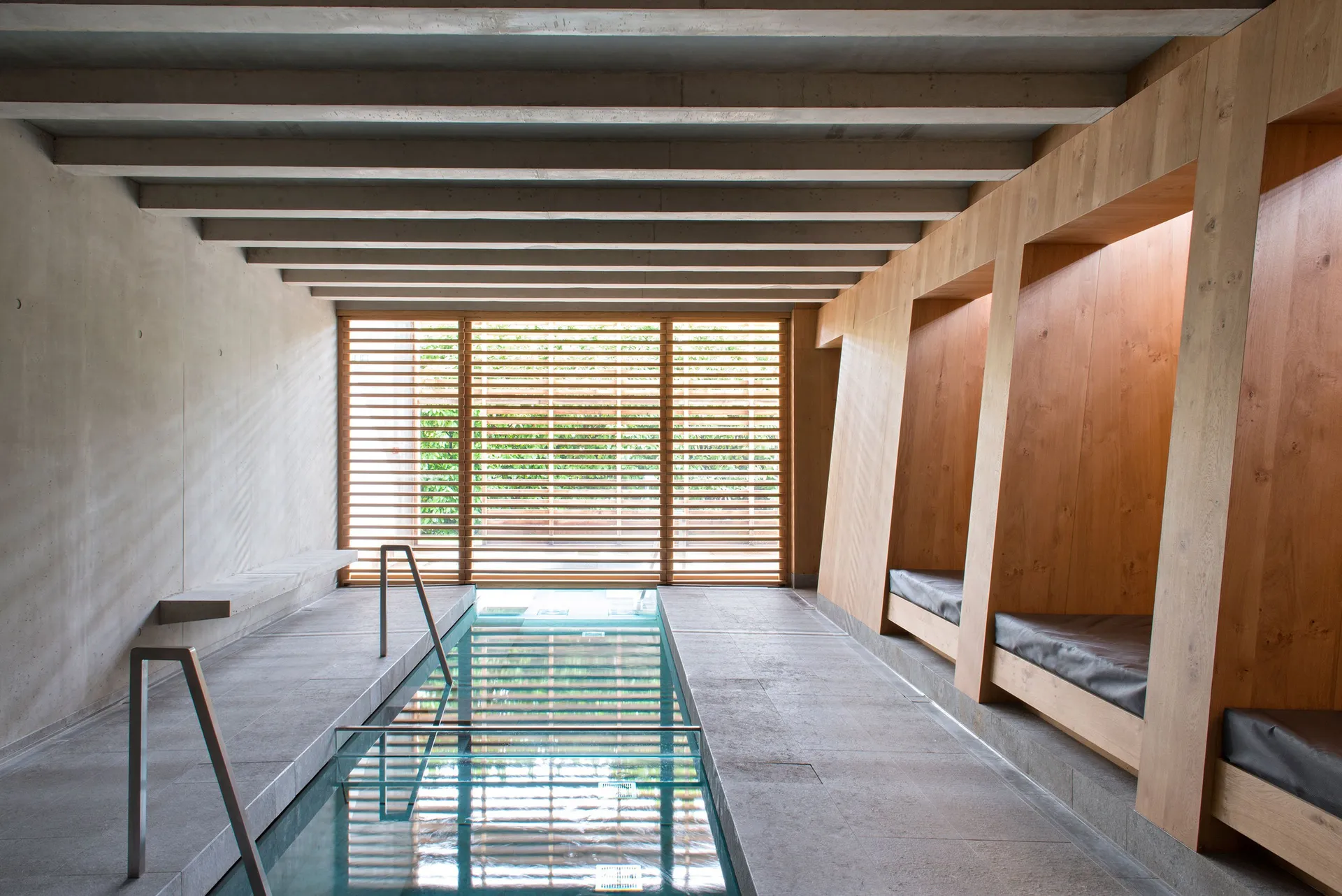 An indoor minimalist spa with concrete walls and wooden benches.