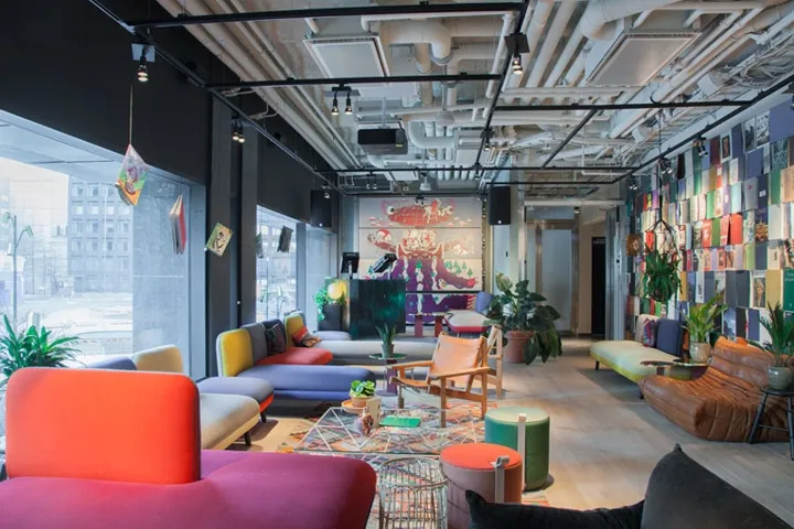 Contemporary office lounge with colorful furniture, plants, and artistic wall decorations.