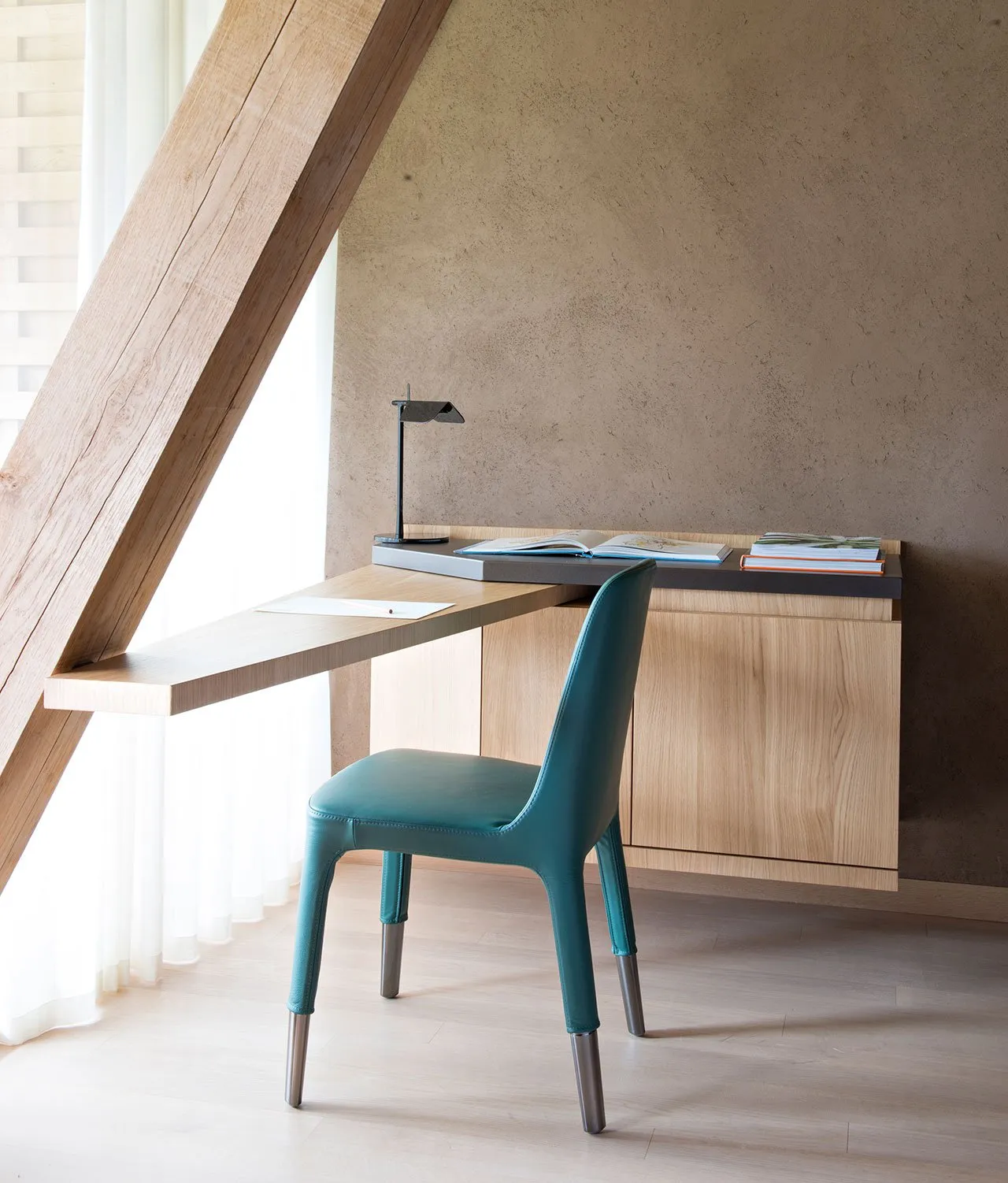 A minimalist modern workstation with a wooden finish, featuring a desk, a green chair, and a lamp.