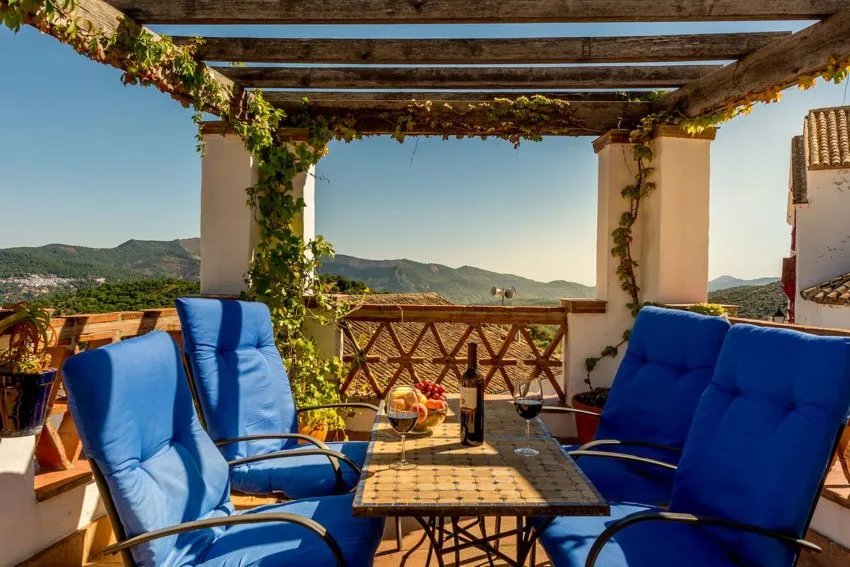 Outdoor lounge area with blue cushioned chairs, wooden pergola, and scenic mountain view.