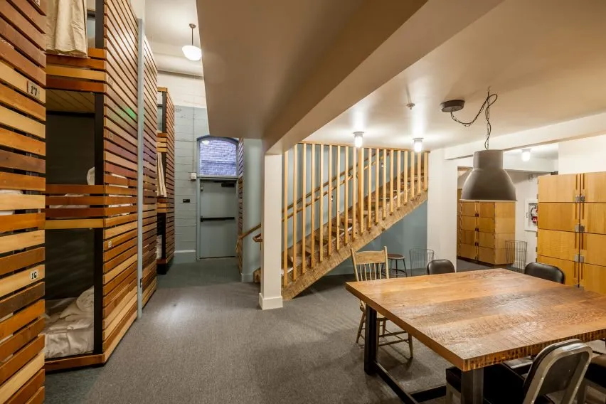 An industrial-style dormitory room with wooden bunk beds and a wooden staircase.