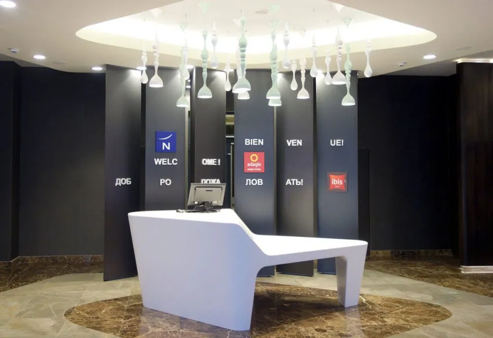 A minimalist hotel reception area with a sleek white desk, black walls, and modern light fixtures.