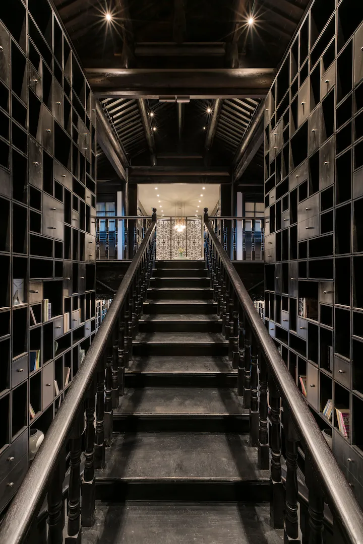 An indoor staircase surrounded by metal shelves filled with books, leading to a brightly lit area.