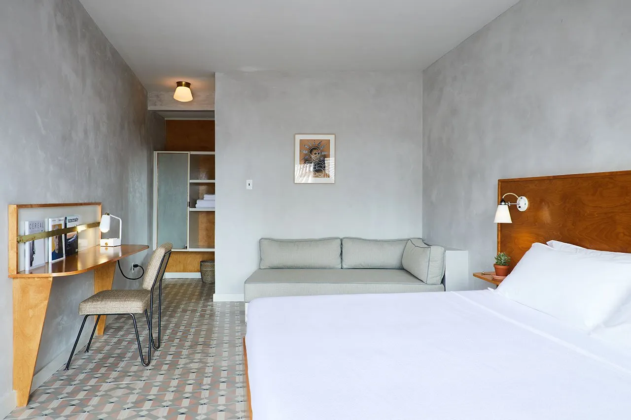 Modern minimalist bedroom featuring concrete walls and floor, a white bed, and a grey couch.