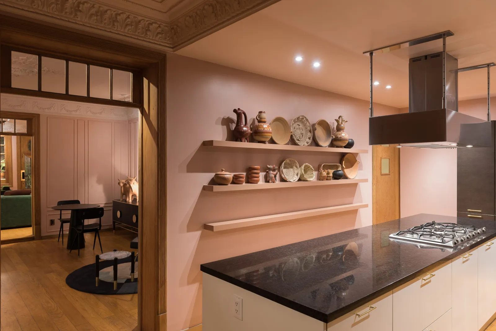 A modern minimalist kitchen with pink walls, white cabinets, and black countertops, featuring decorative pottery on shelves a