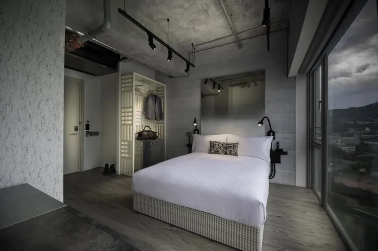 A modern industrial bedroom with concrete walls, flooring, and minimalist furniture.