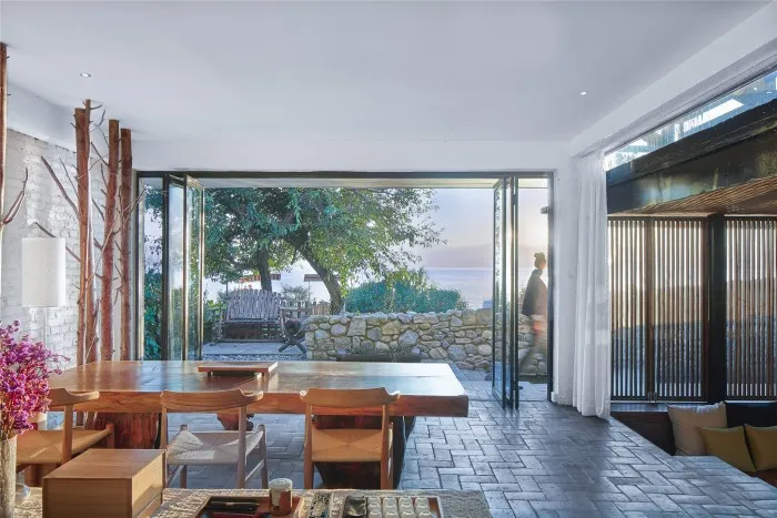 Dining room with minimalist design, wooden table and chairs, glass doors leading to outdoor seating area.