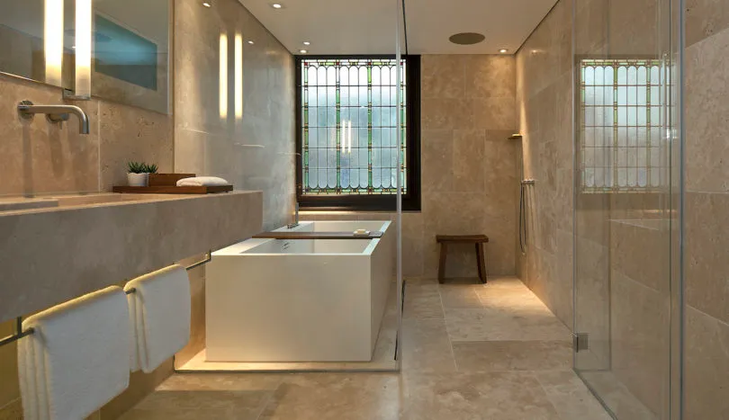 Modern minimalist bathroom with marble tiles, white bathtub, and frosted glass shower doors.