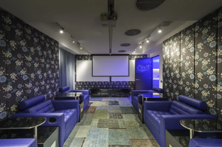 現代休閒室,藍色沙發置於圖案地板上,搭配大型螢幕與藍色燈光。