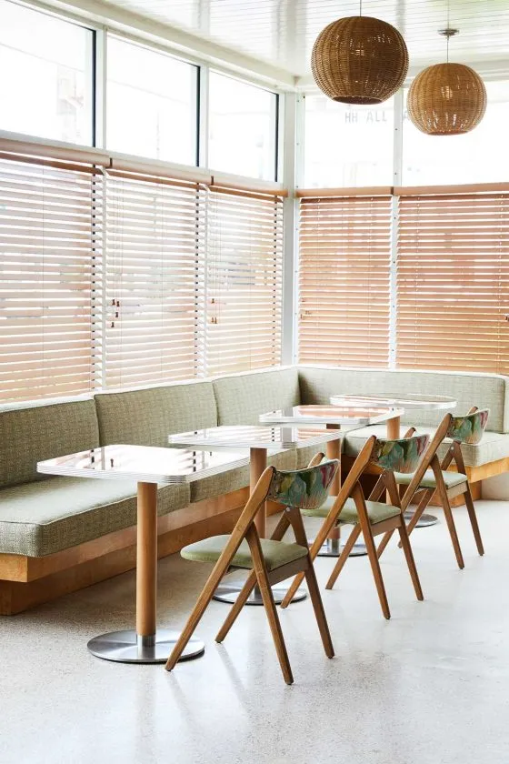 Modern restaurant interior with wooden tables, fabric seating, and glass pendant lights.