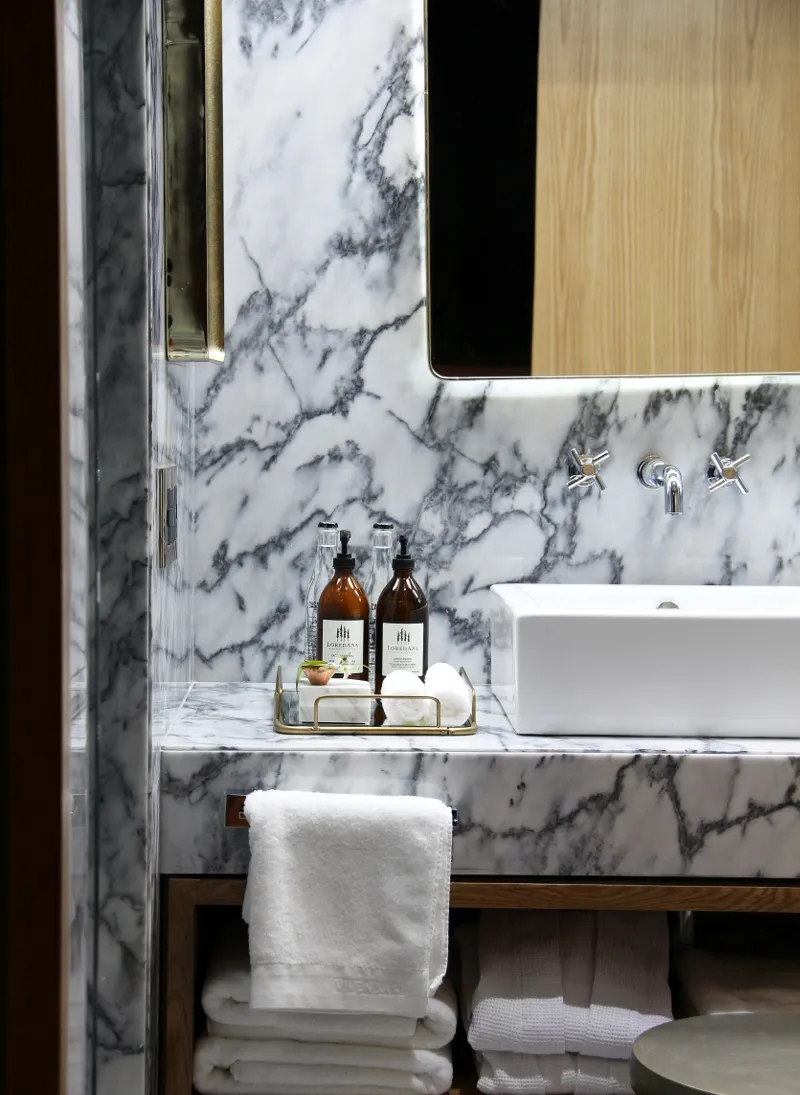A modern bathroom with marble accents, a sink, and neatly stacked white towels.