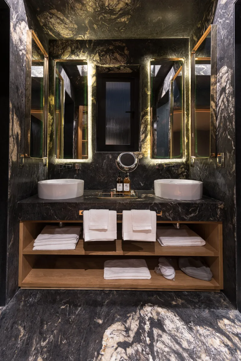 A modern marble bathroom with two sinks, mirrors, towels, and a vanity.