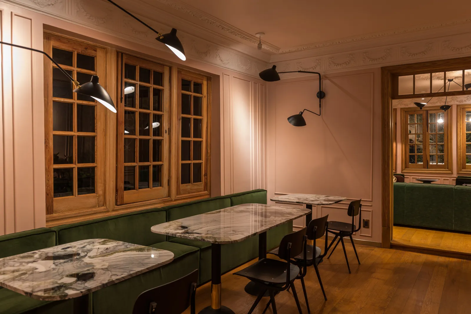 Interior of a modern cafe with marble tables, green upholstered seating, and wooden floors.