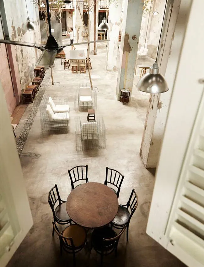 Industrial-style café interior featuring exposed concrete flooring, minimalist white furniture, and sparse lighting fixtures.