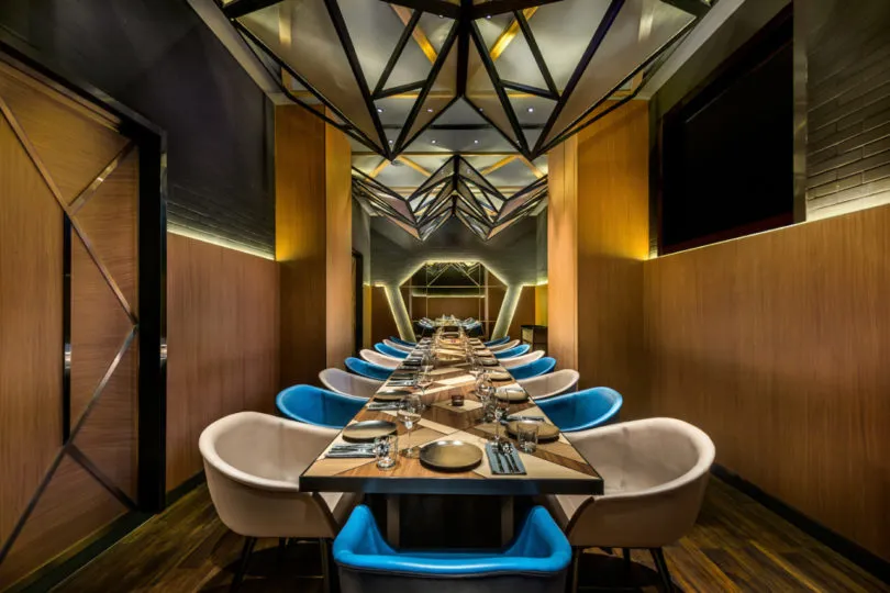 Long dining table with blue and white cushioned chairs in a modern industrial restaurant setting