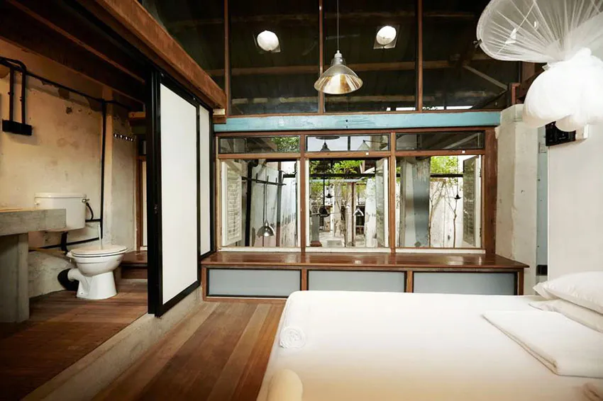 Minimalist bedroom with wood flooring and furnishings, featuring a bed and bathroom area.