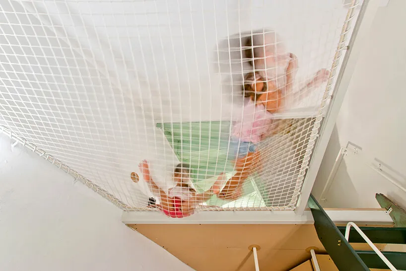 A young child climbing through a safety net in a children's room play area.