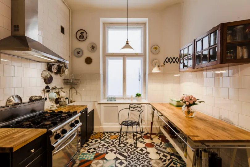 An industrial-style kitchen with patterned tiled flooring, a black stove, wooden countertops, and hanging pendant lights.