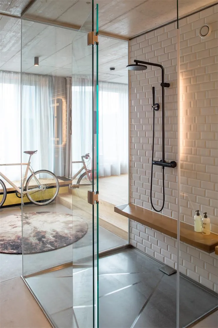 A minimalist bathroom with glass shower enclosure, wooden shelf, and white ceramic tiles.