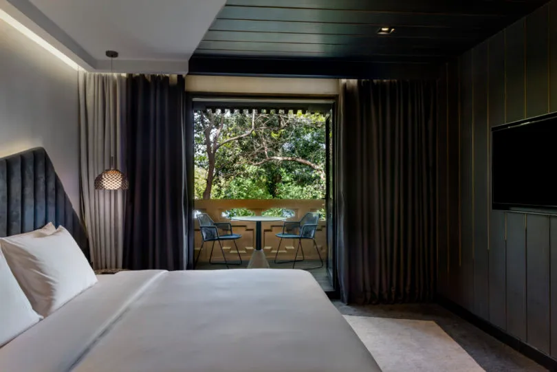 Clean, well-designed minimalist bedroom with grey curtains, a bed with a grey headboard, a small table with two chairs on a b