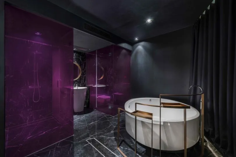 A modern bathroom featuring a white oval bathtub, dark marble tiles, and purple glass walls.
