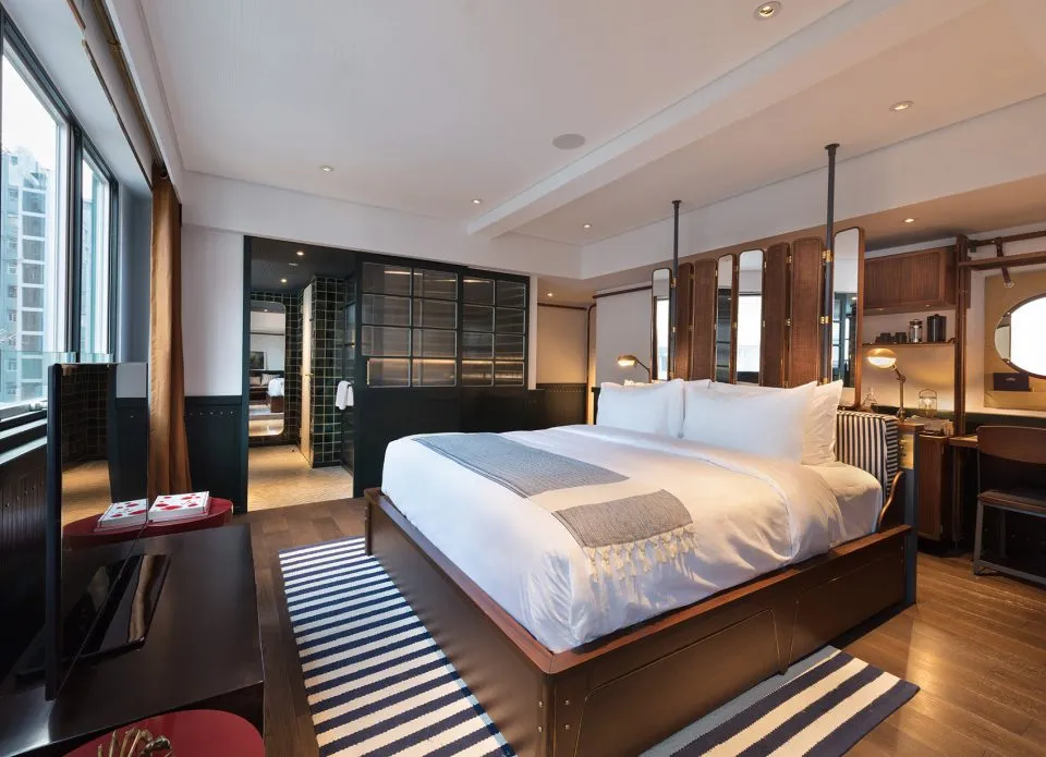 A modern bedroom with a wooden bed frame, white bedding, and striped rug.