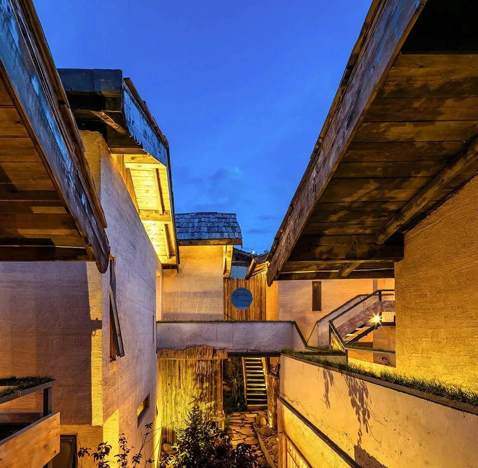 A modern house with wooden and concrete exterior, featuring a narrow alleyway at dusk with warm lighting.