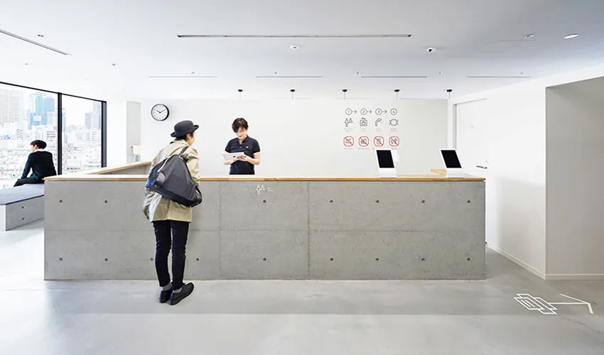 A modern office entrance featuring a concrete and wood reception desk with a digital clock and signage.