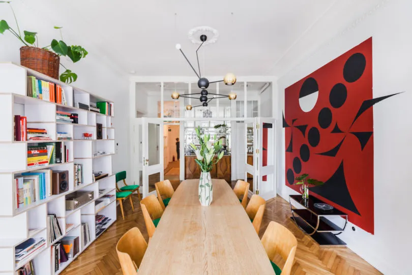 Modern dining room with wooden table and chairs, white walls, and red geometric wall art