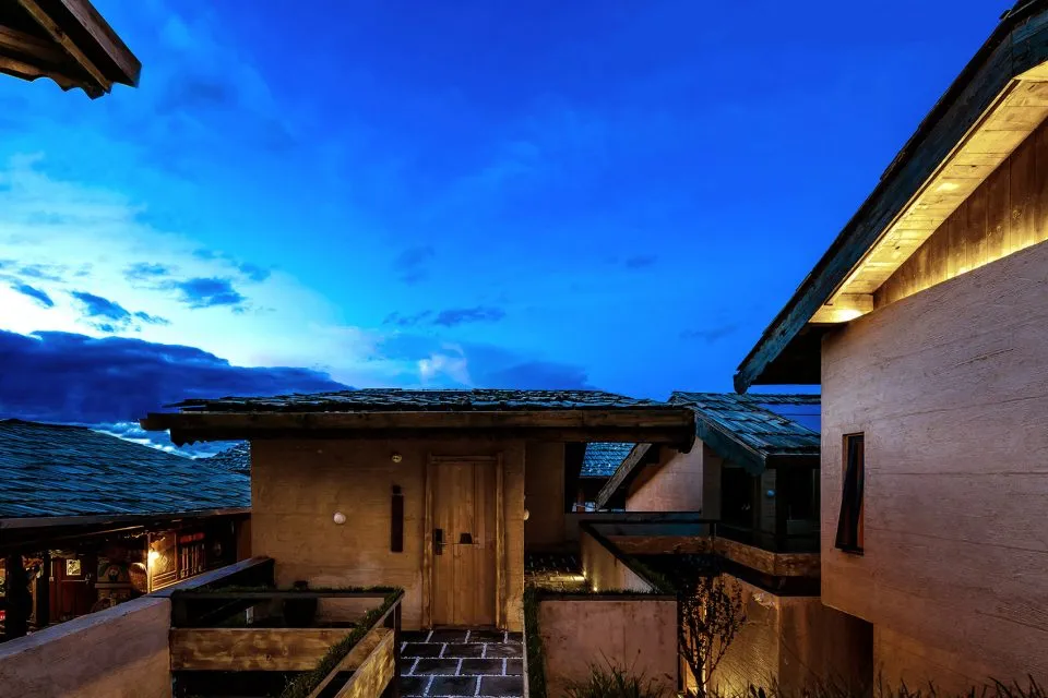 A residential building exterior at night with wooden panels and illuminated stone pathway.