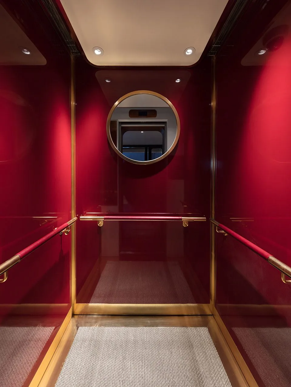 A red metallic elevator interior with glass walls and a circular mirror on the wall.