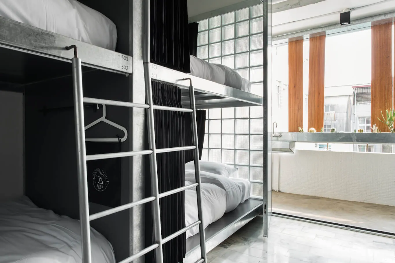 Metallic bunk beds with white bedding in an industrial-style hostel bedroom