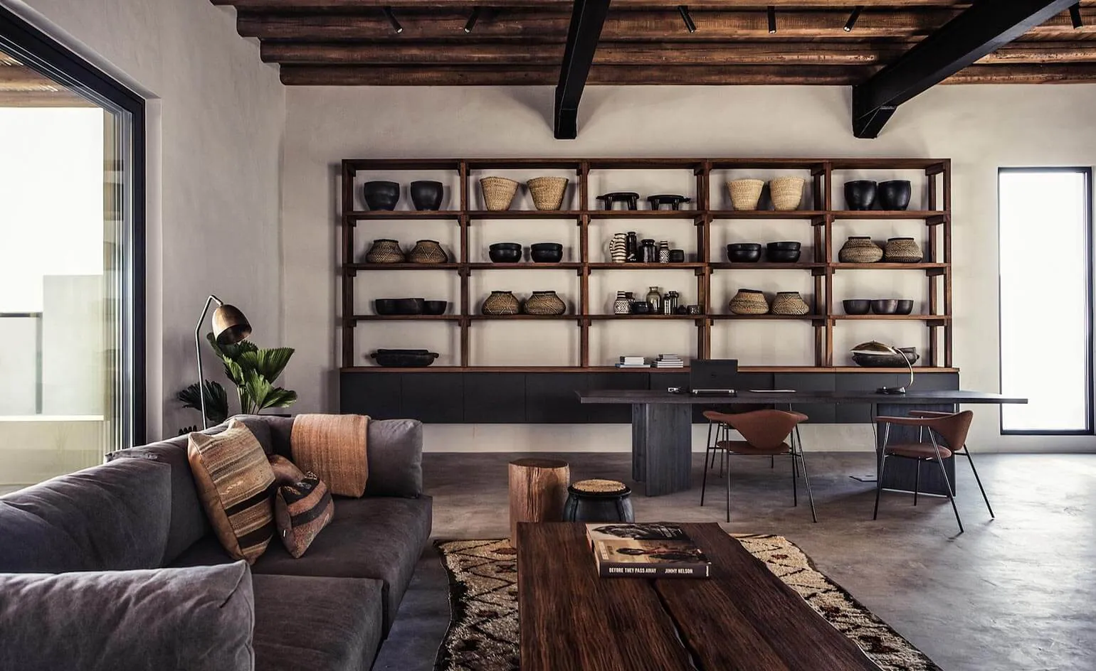 A modern industrial living room featuring wooden shelves, a gray sectional sofa, and a concrete floor.