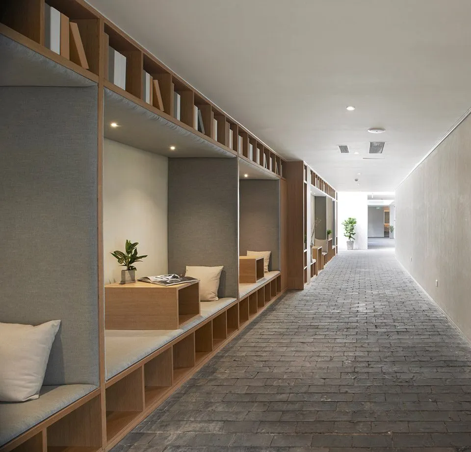 A minimalist corridor workspace with wooden shelves, a desk, and seating area.