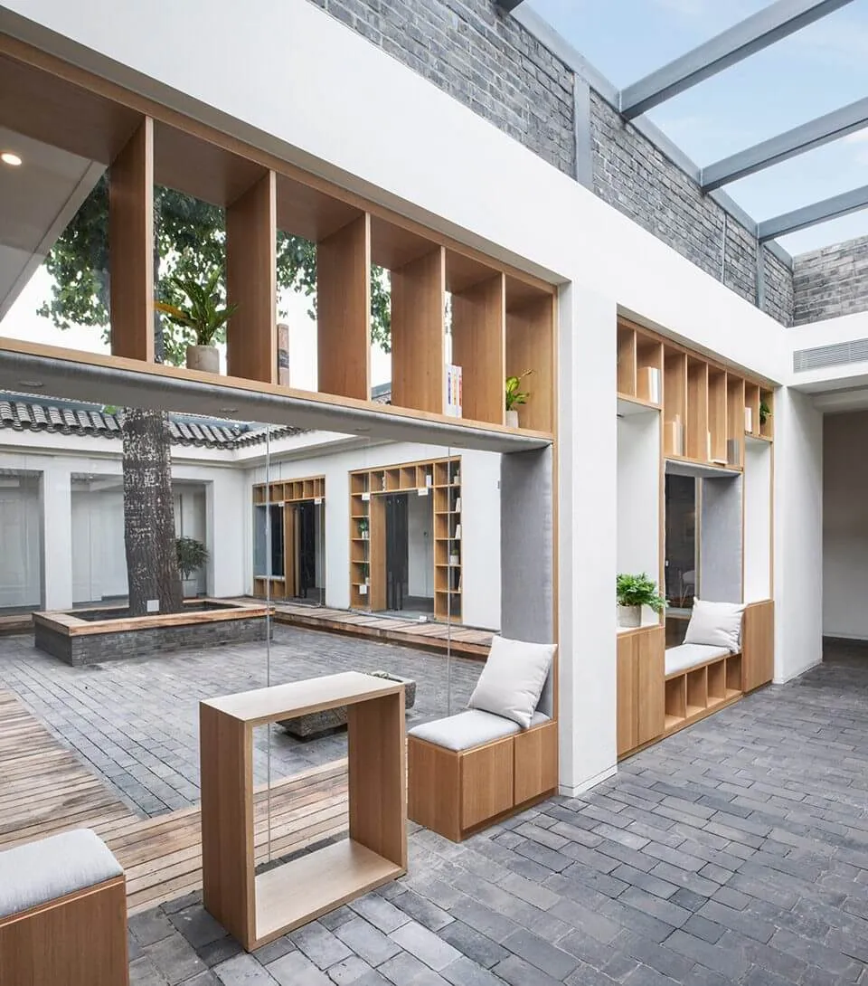 A minimalist courtyard library featuring wooden shelves, concrete pavers, and plants.