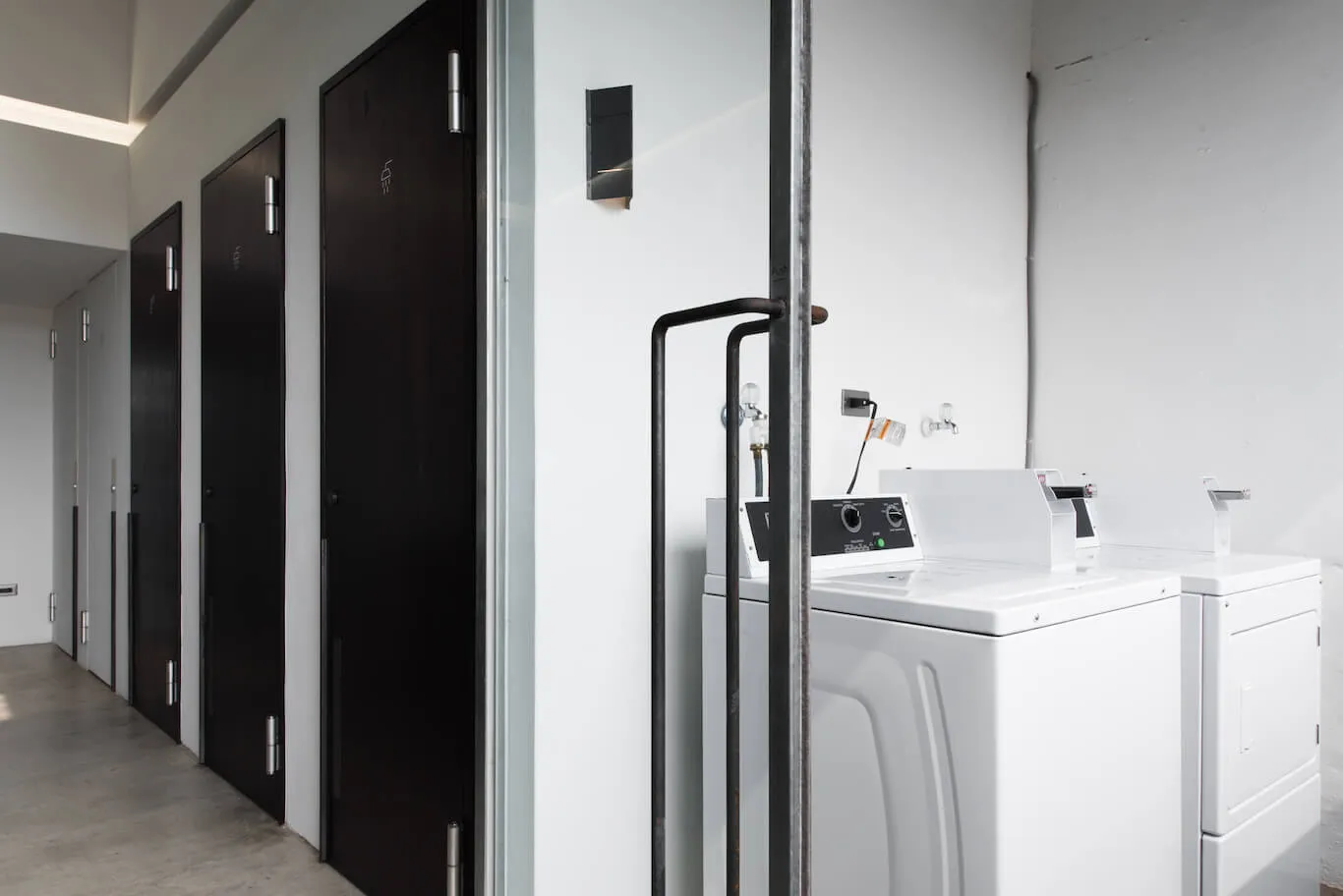 A minimalist laundry room with white appliances and dark wooden doors.