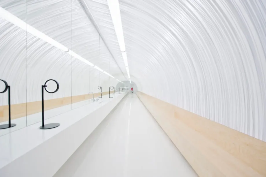 A minimalist white corridor with wooden accents and linear lighting.