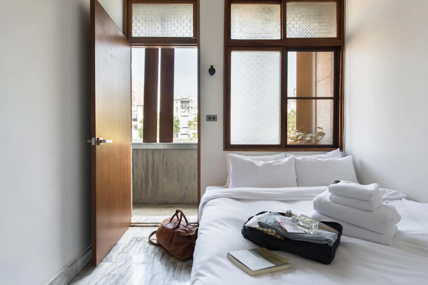 Modern white bedroom with minimalist design, glass windows, and fabric furniture.