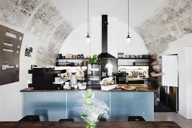 A modern coffee shop interior with concrete walls, a wooden counter, and industrial pendant lights.
