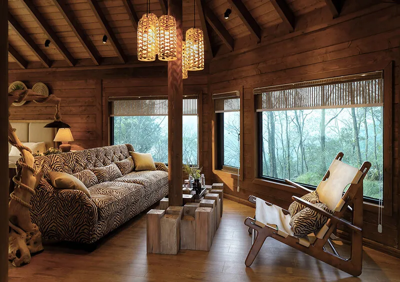 A cozy living room with a wooden ceiling, log walls, and a comfortable sofa with a zebra print cover, surrounded by large win