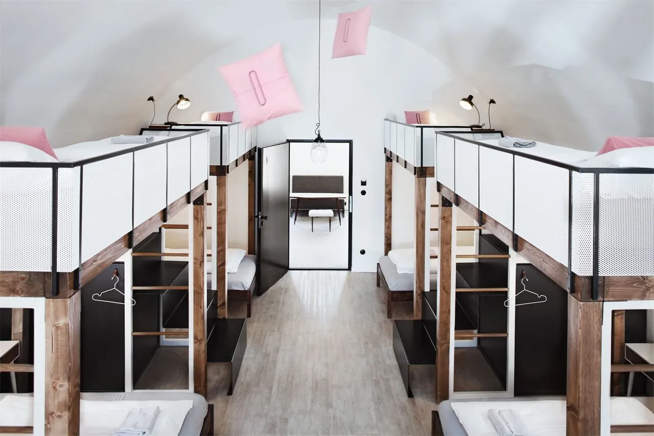 A minimalist bedroom with wooden bunk beds, white bedding, and hanging pink pillows.