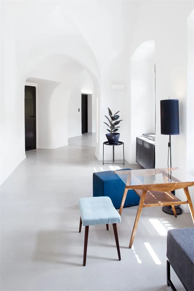 Modern minimalist interior with a concrete floor, blue ottoman, and wooden lamp.