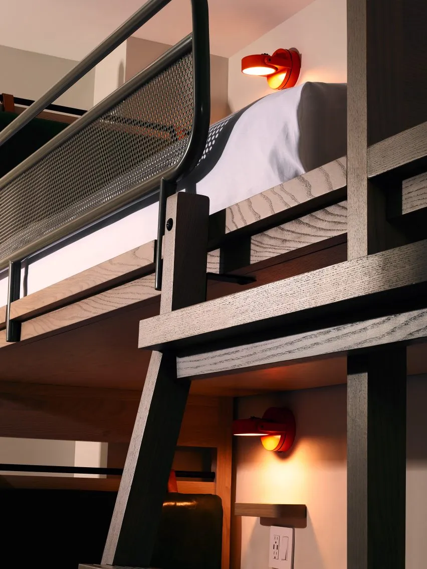 A minimalist, industrial-style bedroom featuring a wooden bunk bed with cabinets underneath and a modern red lamp.