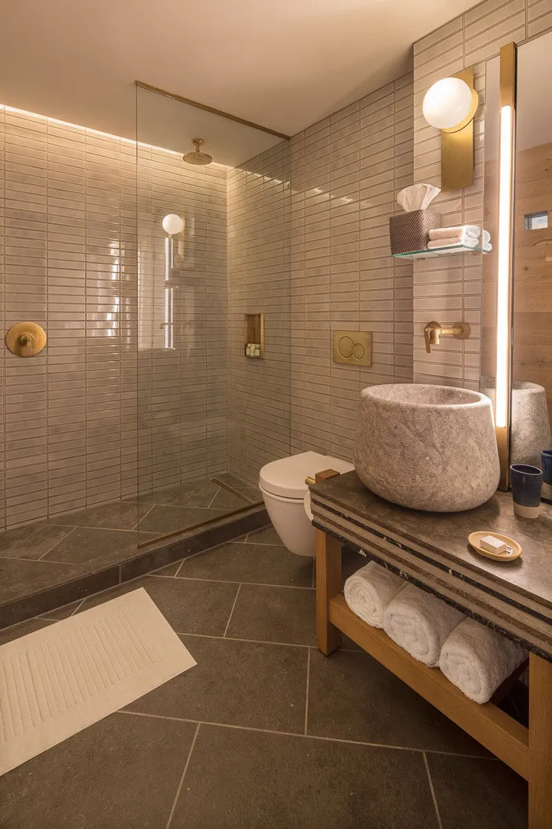 A modern minimalist bathroom with a stone sink, white toilet, and glass shower enclosure.