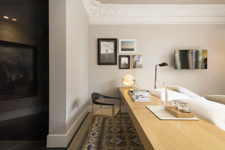 A minimalist bedroom with a wooden desk, black chair, framed pictures, and a bed.