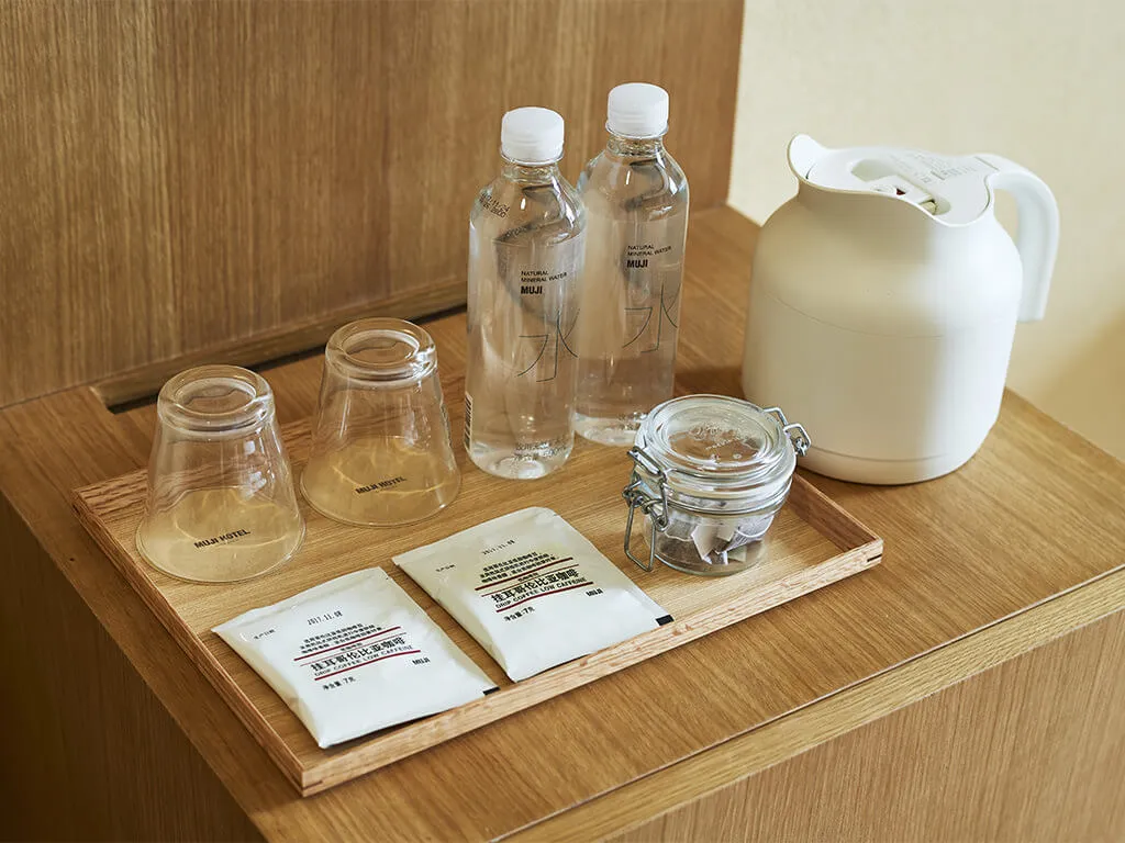 Luxurious, minimalist hotel room amenities including wooden tray, clear plastic cups, and plastic water bottles.