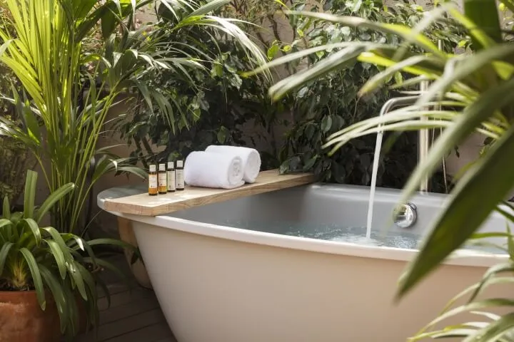A modern bathroom featuring a white bathtub on a wooden shelf surrounded by plants.